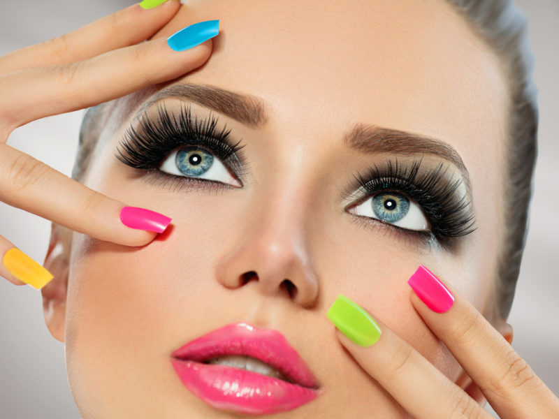 Beauty girl face with colorful nail polish. Manicure and makeup